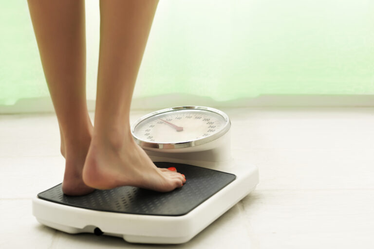 Woman standing on a scale representing differences between lipedema and normal weight gain.