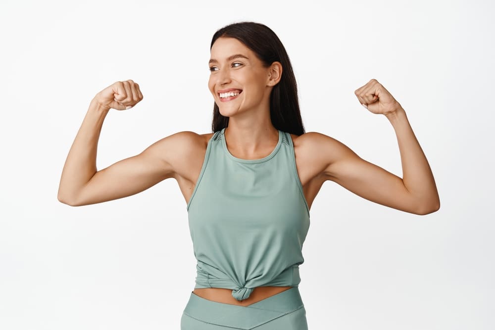 Fit woman flexing her arms, representing arm lift surgery for smoother upper-arm contours in Palm Beach Gardens.