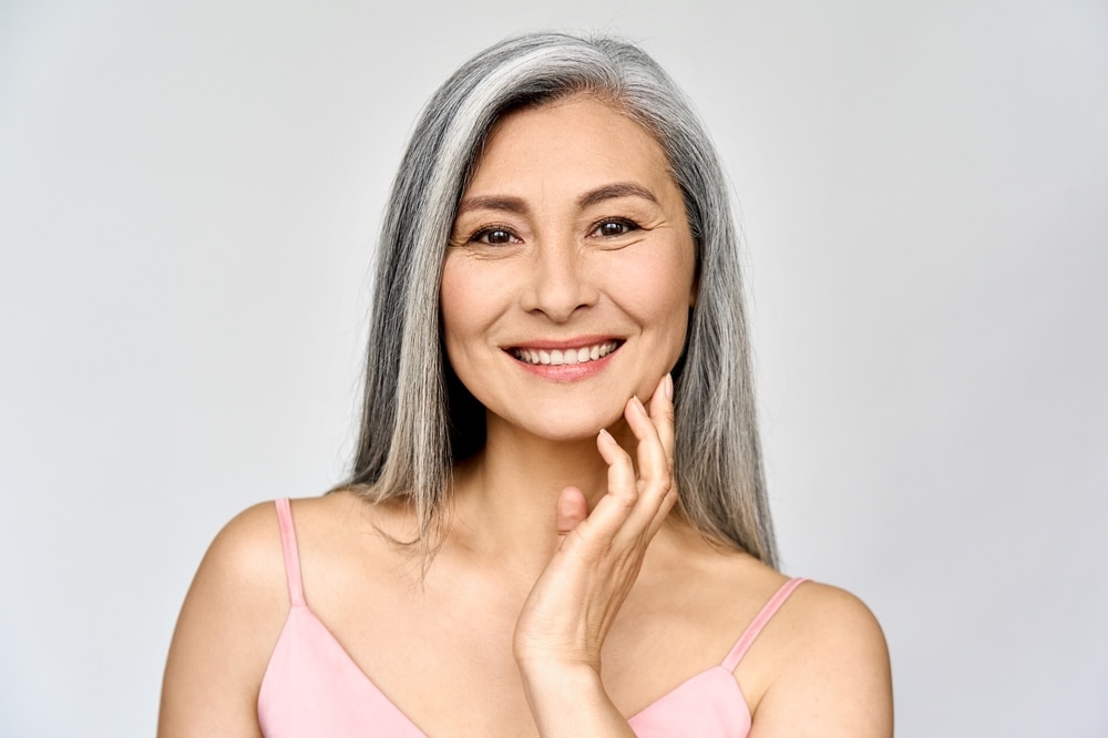 Smiling mature woman touching her cheek, representing midface lift and cheek rejuvenation in Palm Beach Gardens.