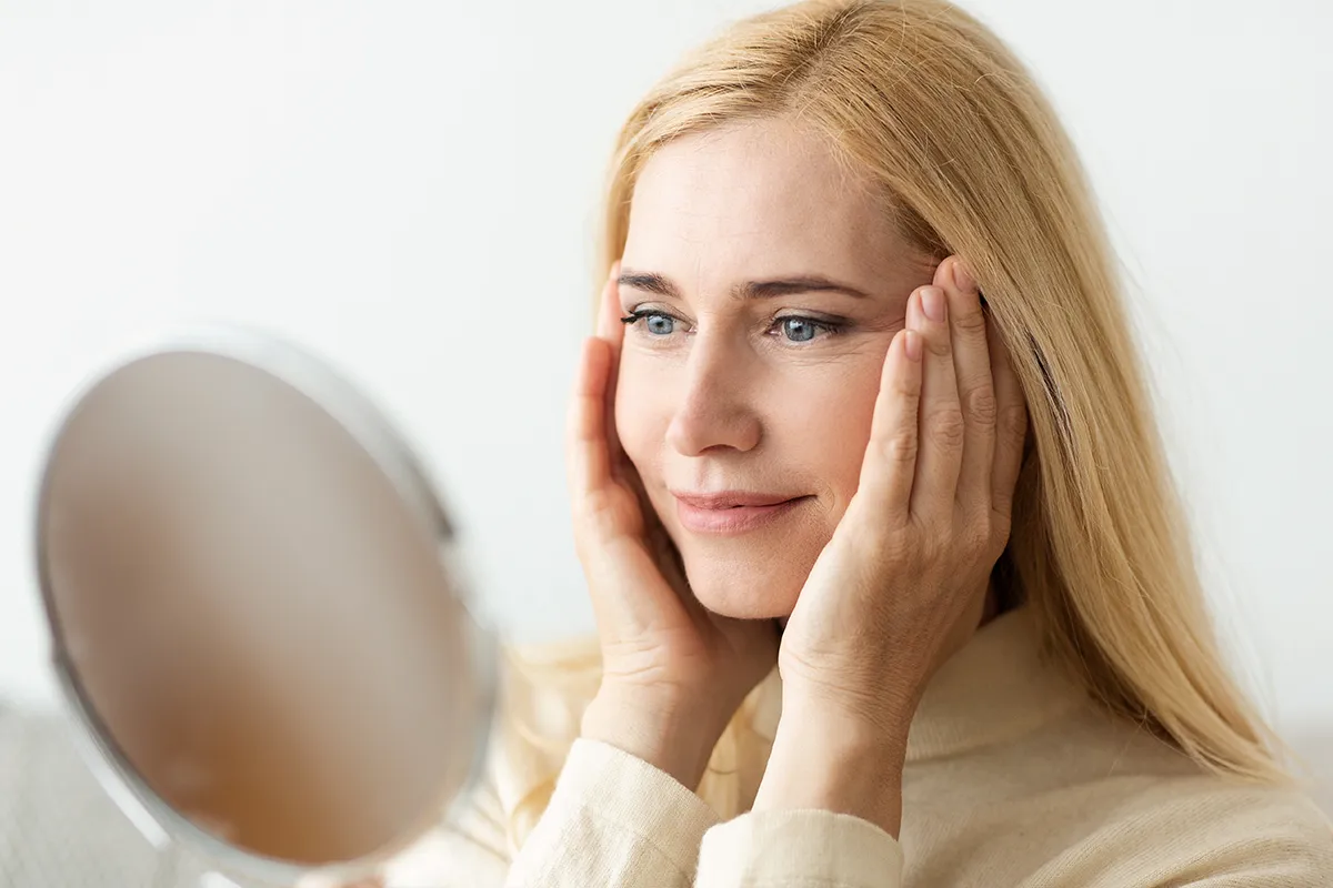 Mature woman examining facial changes in a mirror.