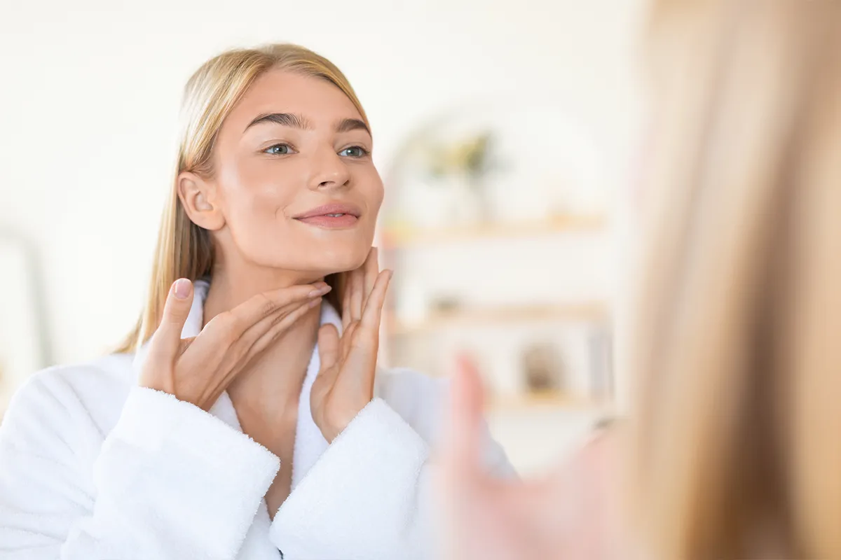 Woman examining her jawline and neck in a mirror.
