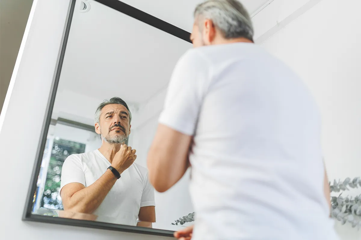 Mature man examining his neck and jawline in a mirror.